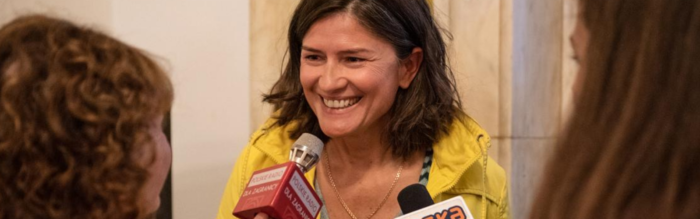 Uśmiechnięta kobieta w żółtej kurtce udziela wywiadu